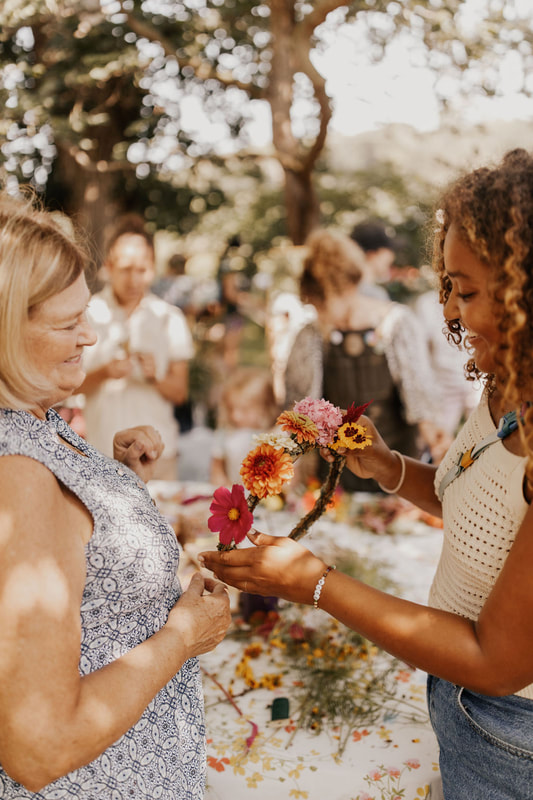 Adults smiling while they assemble a flower crown together during a community flower workshop with District 2 Floral Studio.
