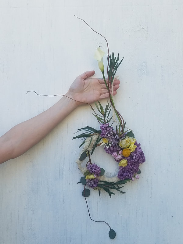 Wild curly willow, asymmetrical wreath with yellows and purple created by District 2 Floral Studio.