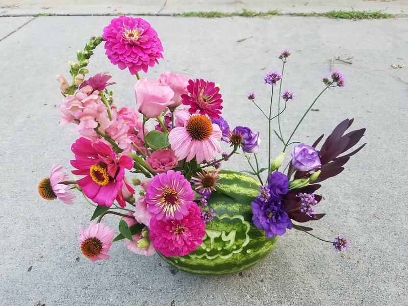 Pink and purple flower arrangement in a carved watermelon by District 2 Floral Studio created with locally grown flowers.