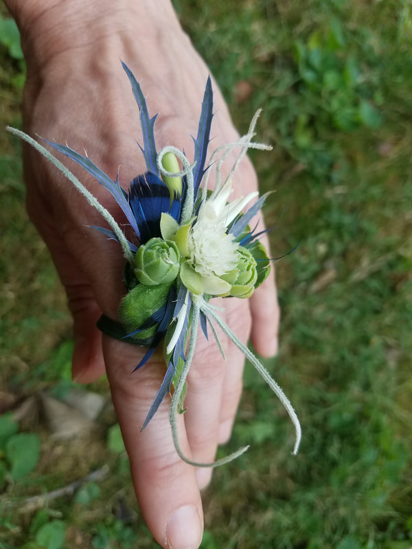 Finger wearing a ring created with locally grown flowers, succulents and a feather created by District 2 Floral Studio.