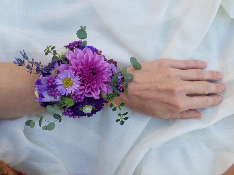 Hand wearing a bright pink and purple wristlet corsage created with locally grown flowers created by District 2 Floral Studio.