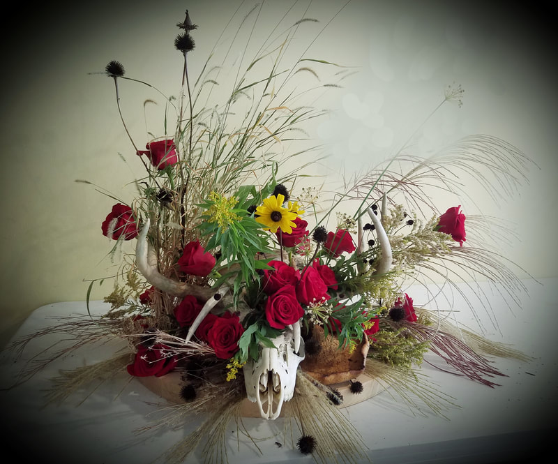 Deer skull with antlers covered in red roses, rudbeckia, and locally grown Nebraska grasses and seed heads. Created by District 2 Floral Studio.