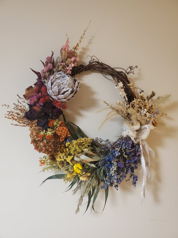 Rainbow colored, asymmetrical wreath created by District 2 Floral Studio with dried flowers.