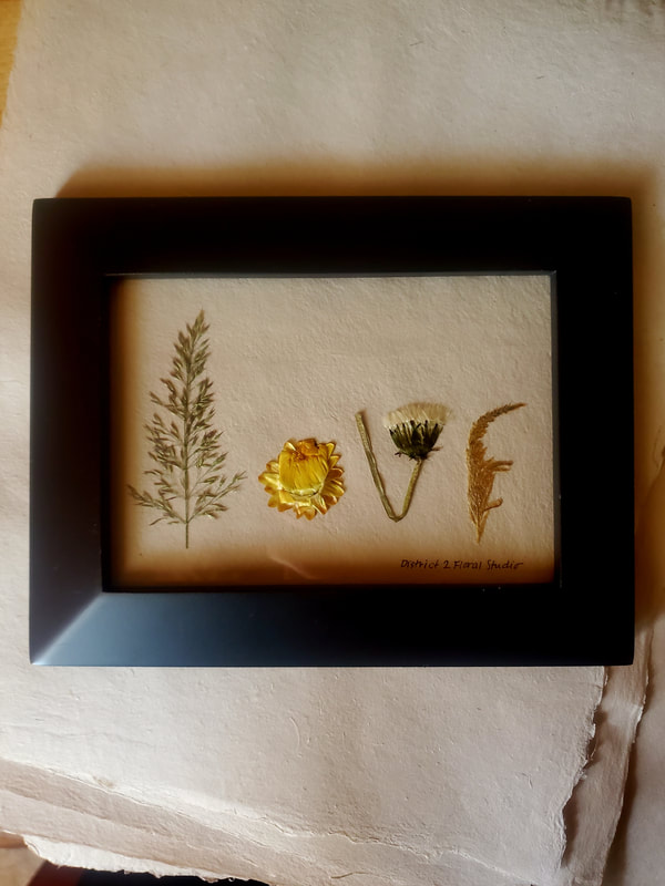Pressed and framed flower preservation by District 2 Floral Studio with each flower shape spelling the word LOVE.
