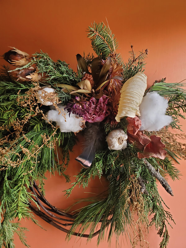 Seasonal winter symmetrical wreath created by District 2 Floral Studio with locally grown Nebraska evergreens, feathers, garlic bulb and dried flowers.