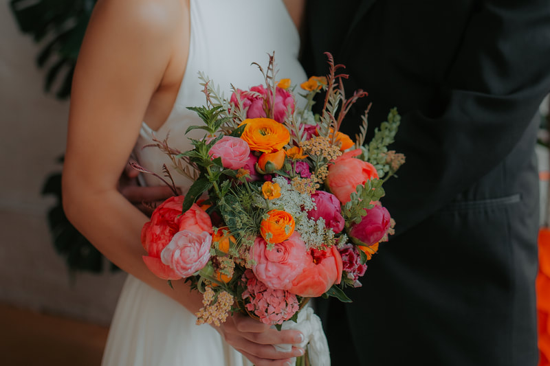 Bride holding a bright pink and orange spring wedding bridal bouquet by District 2 Floral Studio using local and American-grown flowers.