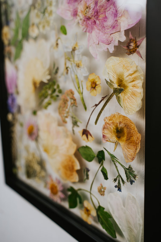 Up close of a pressed flower preservation piece by District 2 Floral Studio in a custom black frame.