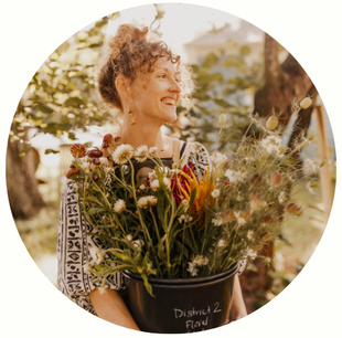 Holly smiling as an adult holding a bucket of fresh, locally-grown flowers.