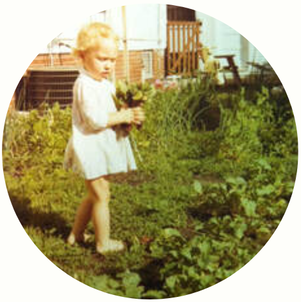 Holly standing in their home garden as a child holding a bunch of leafy greens in her hands.