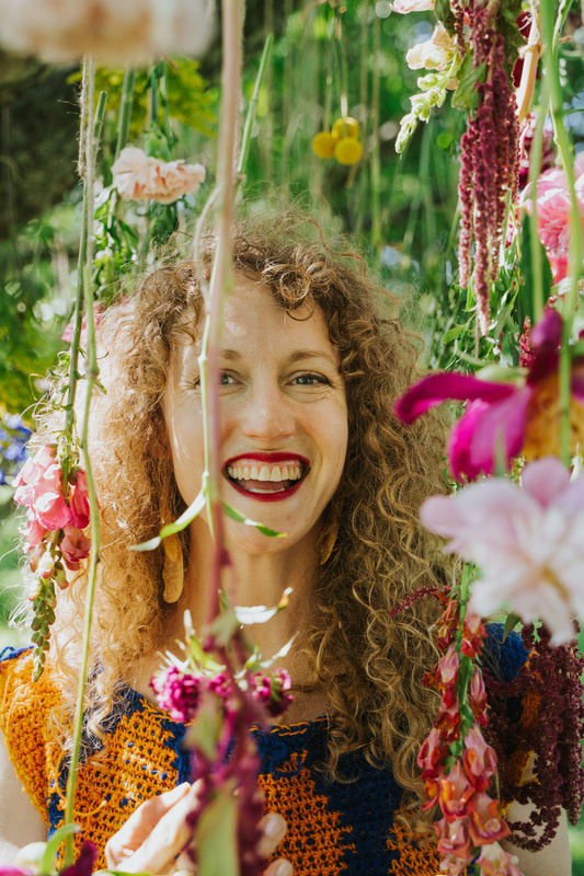 An adult smiles amidst flowers suspended from branches around their face. Installation by District 2 Floral Studio.