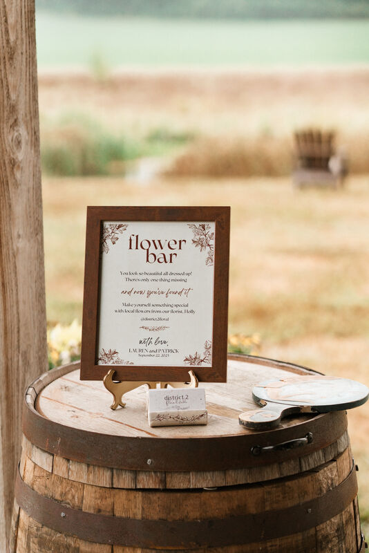 Barrel at a wedding reception with a framed sign on it that reads "Flower Bar".