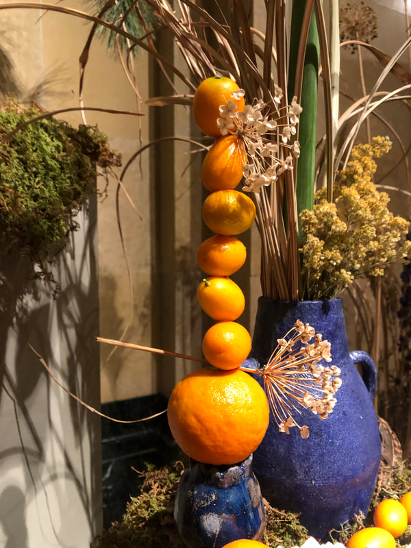Up close view of seasonal winter floral installation by District 2 Floral Studio at a Cathedral with locally grown Nebraska evergreens, grasses, dried flowers, amaryllis and clementines and hand-built blue ceramic vases.