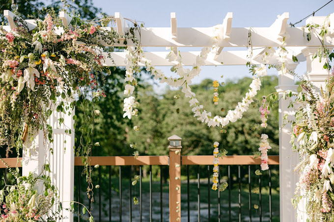 White pergola is covered in locally grown Nebraska florals. Foam-free installation created by District 2 Floral Studio with floral garlands.