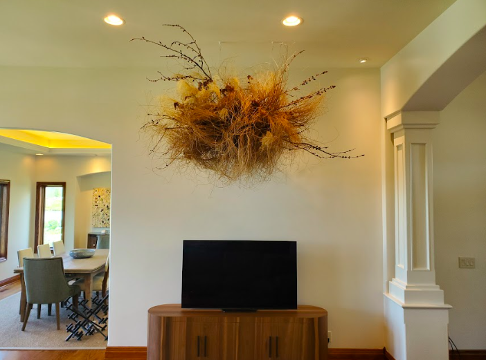 Branches and locally grown Nebraska dried grasses form a cloud created by District 2 Floral Studio that is suspended from the ceiling above a TV in a spacious living room. 