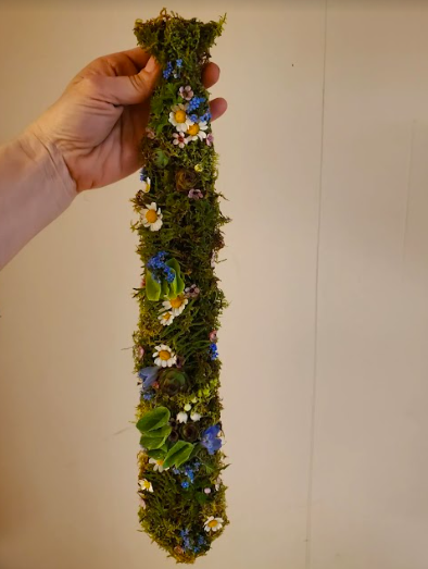 Hand holding a formal tie that is covered in moss and locally grown flowers created by District 2 Floral Studio.
