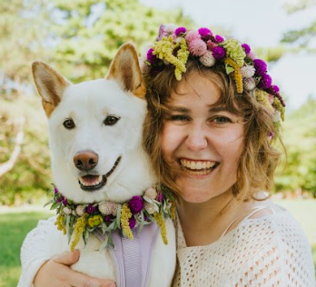 Human wearing a floral crown hugging their white dog wearing a floral collar, both created by District 2 Floral Studio with locally grown floral.
