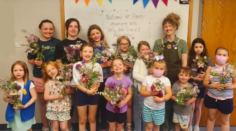 Group of youth each smiling and holding a flower arrangement they created during a District 2 Floral Studio flower design workshop.