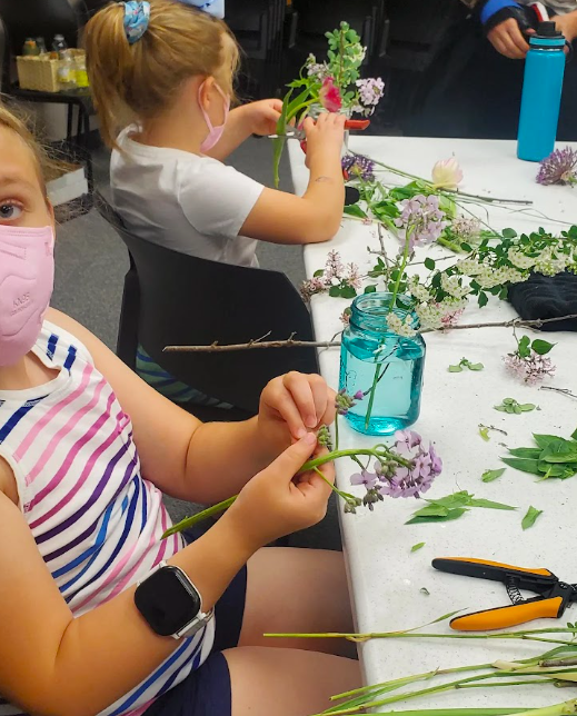 Youth each holding flowers while creating a flower arrangement during a District 2 Floral Studio flower design workshop.