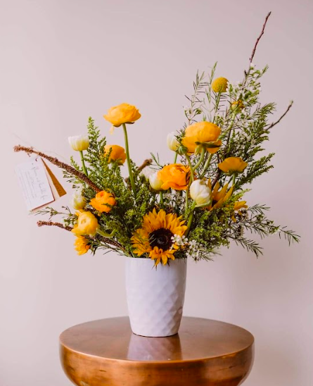 Sunflower and ranunculus flower arrangement by District 2 Floral Studio created with locally grown flowers in a white vase.