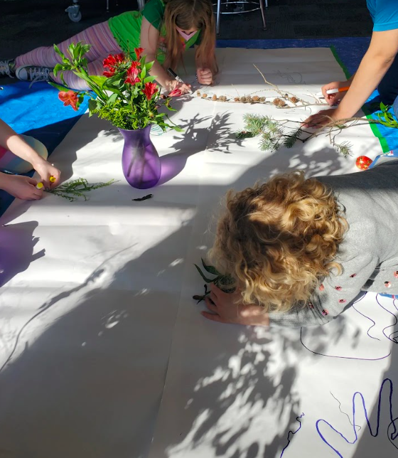 Youth tracing shadow shapes on a large piece of white paper during a District 2 Floral Studio design workshop.