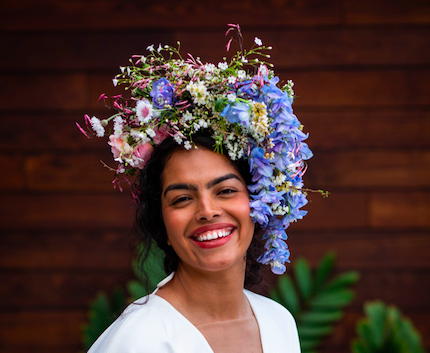 Human smiling wearing an asymmetrical floral headpiece crown  with pink and purple created by District 2 Floral Studio using locally grown flowers.