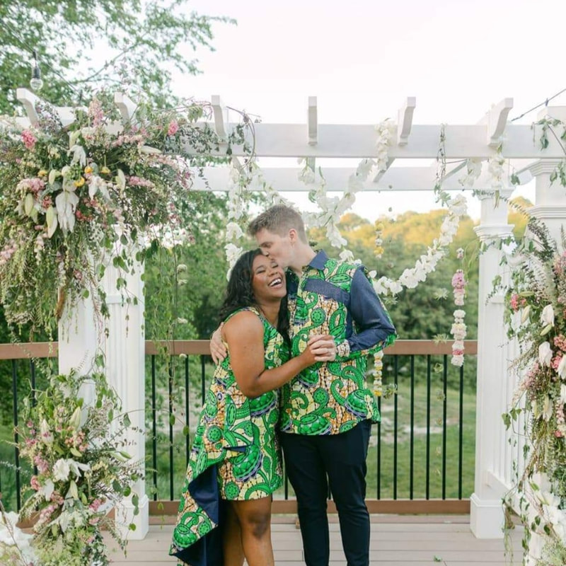Wedding couple embraces under a white pergola that is covered in locally grown Nebraska flowers. Foam-free installation created by District 2 Floral Studio.