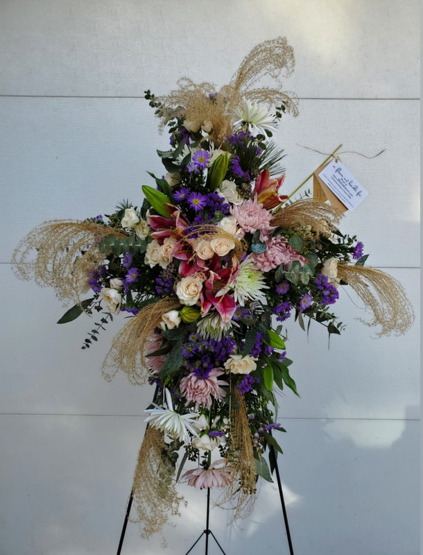 Foam-free cross-shaped floral funeral spray on an easel with pink and purple flowers. Created by District 2 Floral Studio.