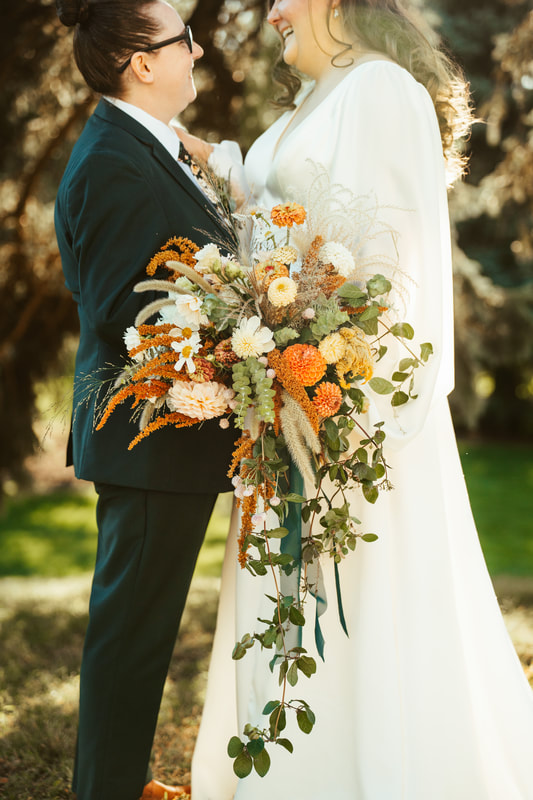 A couple holding a draping ivory, rust and green autumn October wedding bridal bouquet by District 2 Floral Studio using locally-grown flowers.