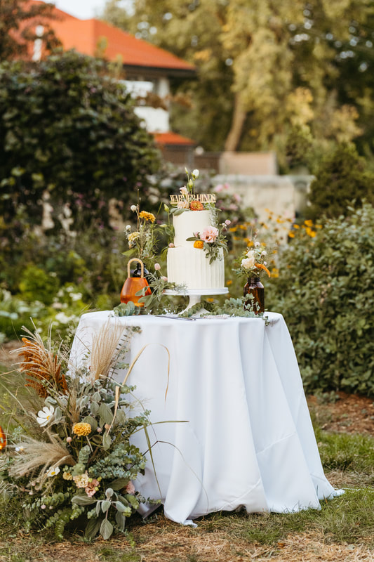 Outdoor wedding cake table with tiered white cake adorned with all locally grown Nebraska flowers. Created by District 2 Floral Studio.