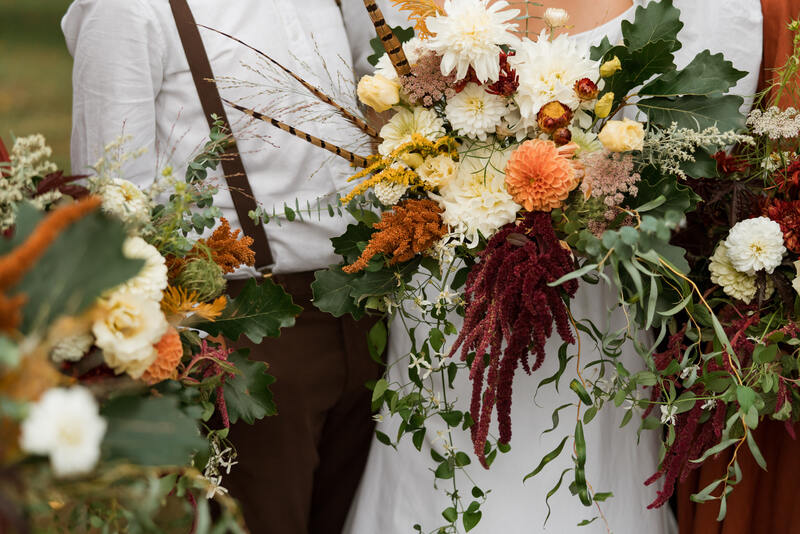 Draping rust orange, ivory and burgundy autumn September wedding bridal bouquet by District 2 Floral Studio using locally-grown flowers and pheasant feathers.