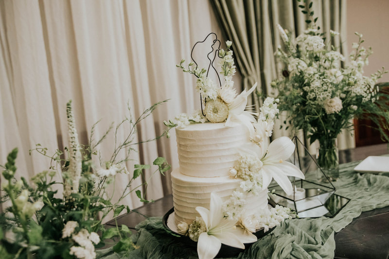 Tiered white wedding cake adorned with locally grown Nebraska flowers. White color palette by District 2 Floral Studio.