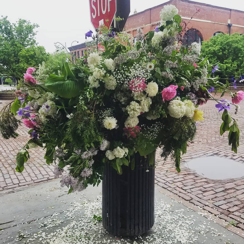 A garbage can acts as a vase with a large eruption of flowers coming from the center of it. Installation by District 2 Floral Studio, inspired by Lewis Miller's "Flower Flashes". 